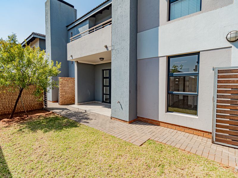 Rear view of the townhouse featuring a paved patio area, small garden, and an upper-level balcony with modern finishes.
