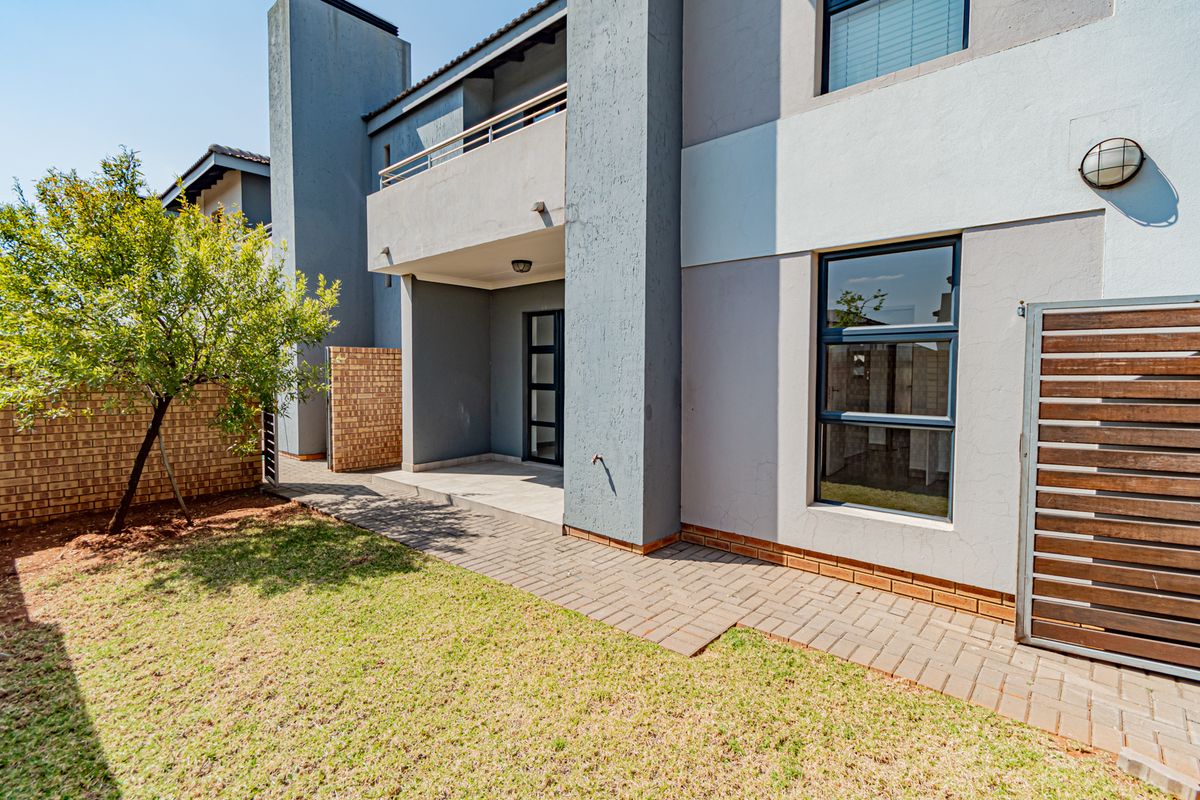 Rear view of the townhouse featuring a paved patio area, small garden, and an upper-level balcony with modern finishes.