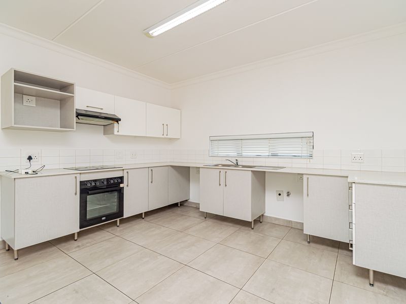 A clean, functional kitchen featuring neutral cabinetry, built-in oven and hob, tiled flooring, and ample counter space in a bright, open layout.
