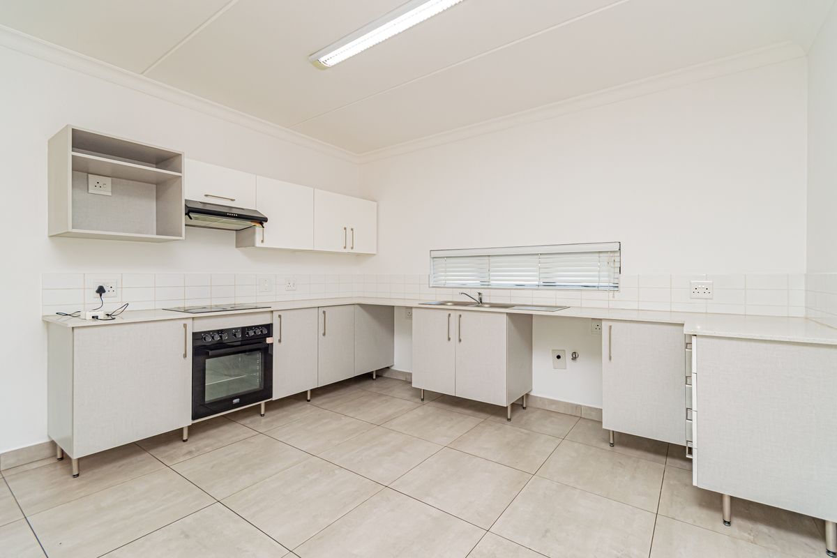 A clean, functional kitchen featuring neutral cabinetry, built-in oven and hob, tiled flooring, and ample counter space in a bright, open layout.
