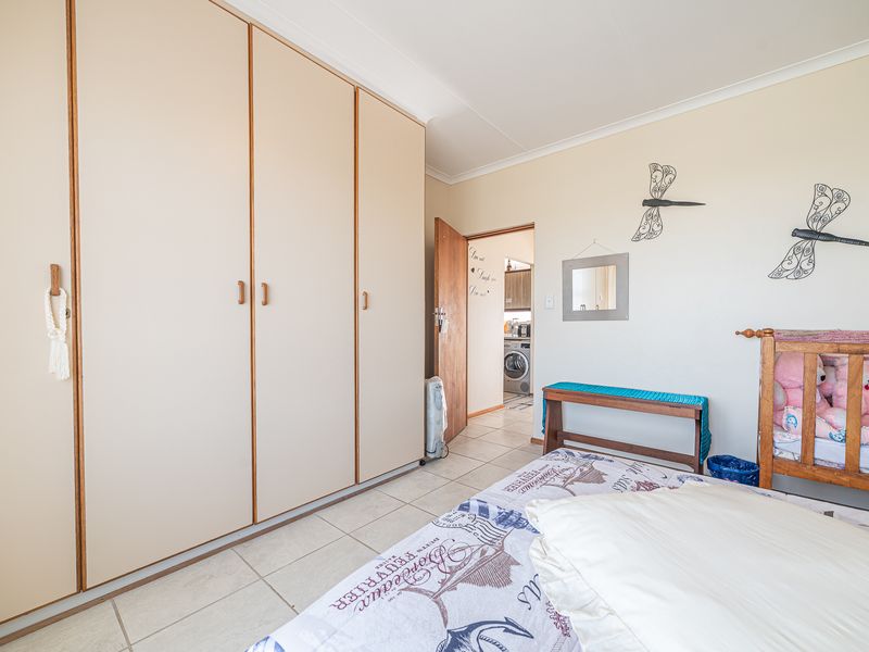 A bedroom featuring built-in cupboards, tiled flooring, and coved ceilings, with a view through the doorway into an adjacent utility area.
