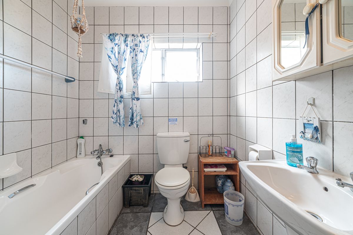 A functional bathroom featuring a bathtub, pedestal basin, and toilet with full-height wall tiling and tiled flooring.