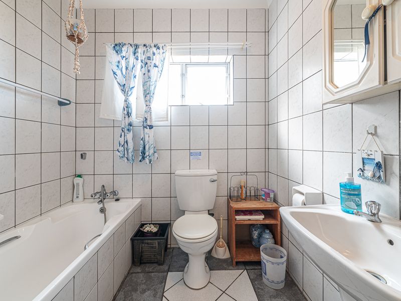 A functional bathroom featuring a bathtub, pedestal basin, and toilet with full-height wall tiling and tiled flooring.