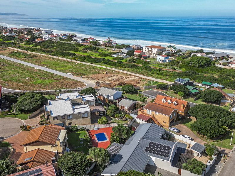 Aerial view of a coastal residential area featuring multiple properties, swimming pools, solar installations, and proximity to the ocean.