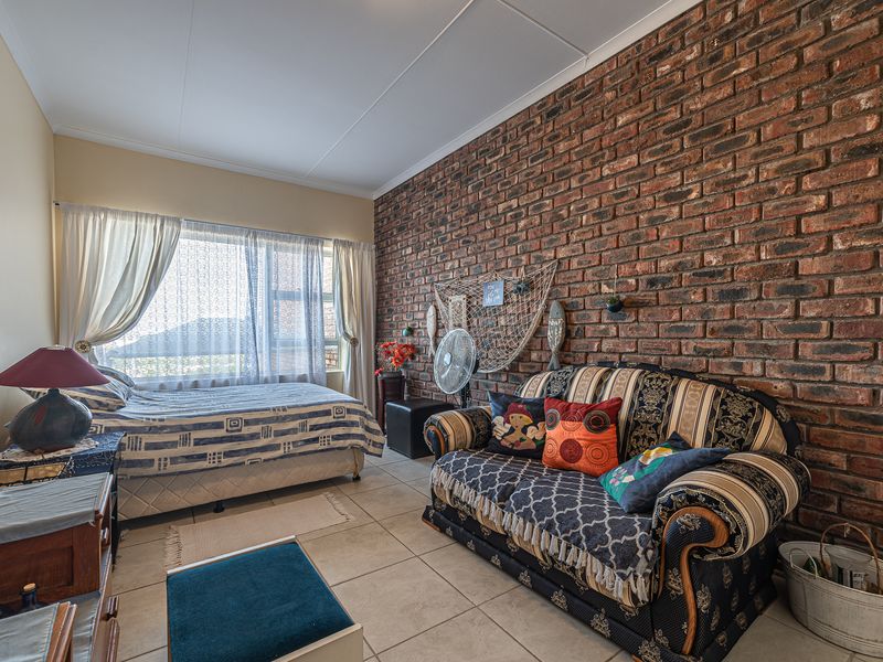 A bedroom featuring an exposed brick feature wall, tiled flooring, and large windows allowing natural light into the space.