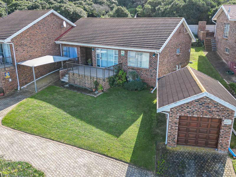 Elevated view of a brick duet property featuring a paved driveway, detached garage, carport, and a raised front patio area with a lawn.