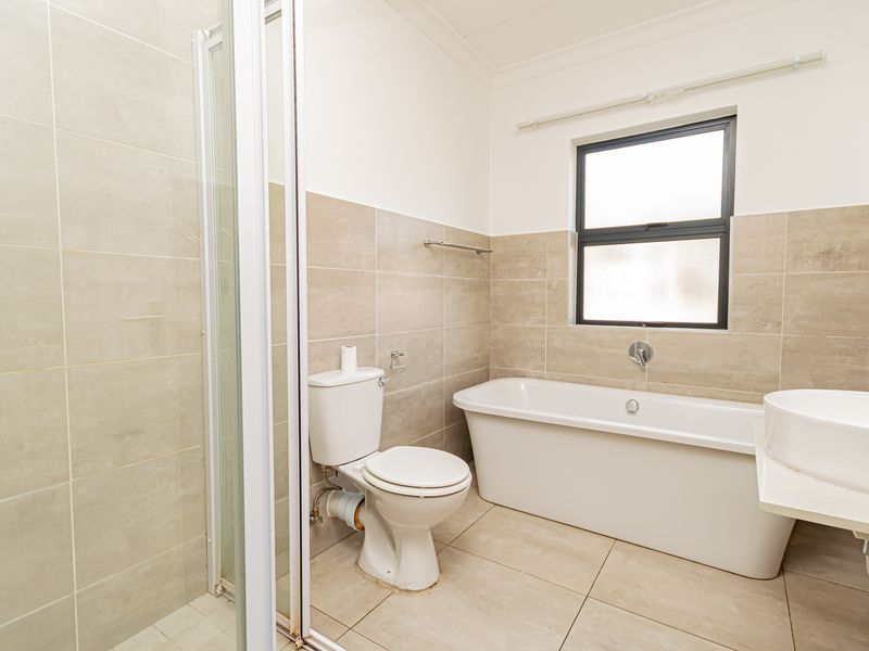 A clean, modern bathroom featuring a separate shower enclosure, a freestanding bathtub, and a wall-mounted basin with neutral floor-to-ceiling tiling.