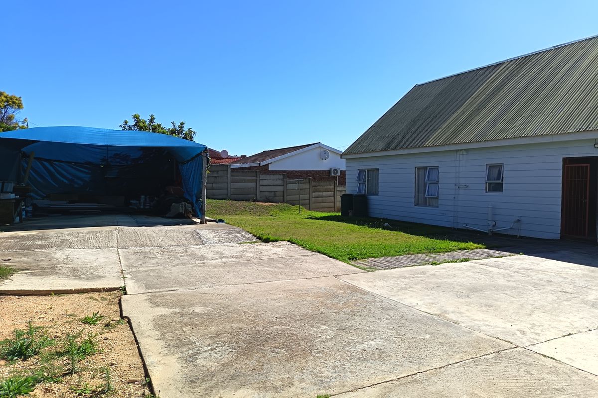 Rear exterior view of the property featuring a large concrete driveway, corrugated metal roofing, and a precast concrete boundary wall.