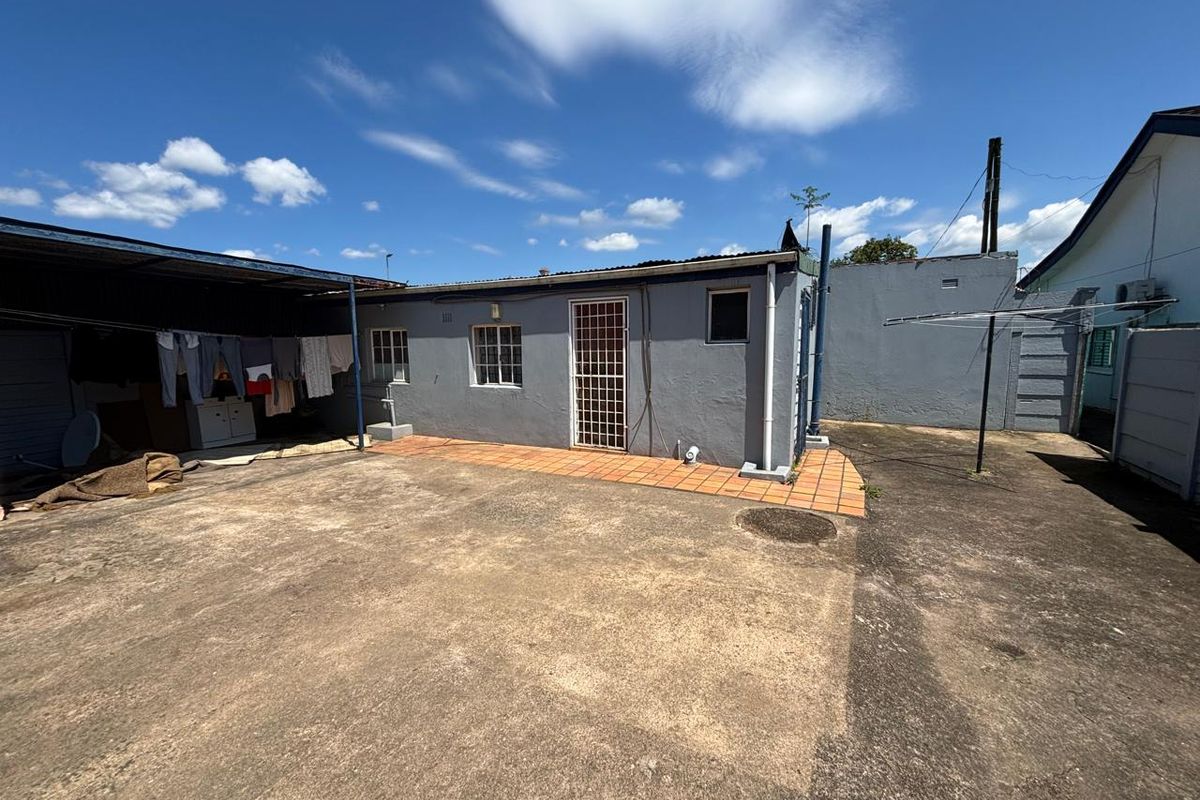 Rear exterior view of the property featuring a concrete courtyard, tiled patio area, and a covered utility space.