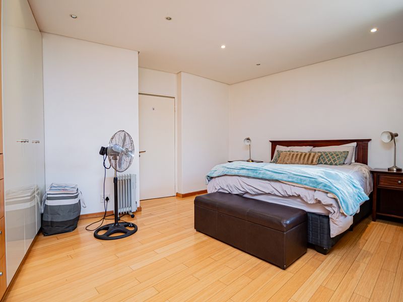 A well-maintained bedroom featuring light laminate flooring, recessed downlighting, and ample built-in cupboard storage.