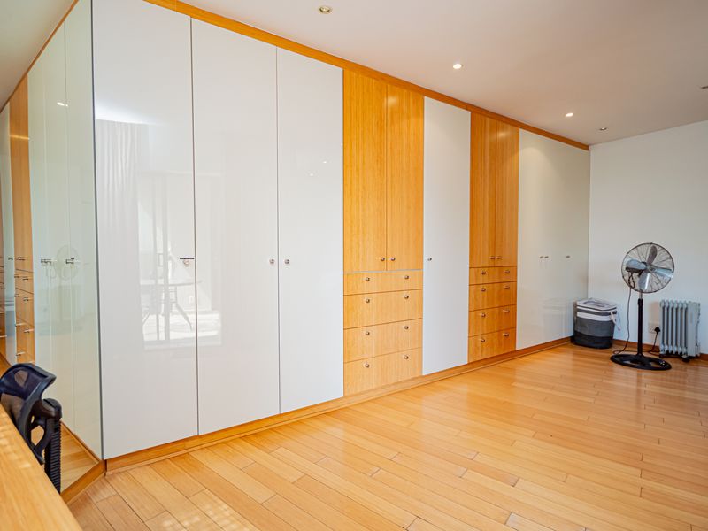 Spacious bedroom featuring extensive floor-to-ceiling built-in cabinetry with a mix of white gloss and wood-grain finishes, complemented by warm wooden flooring.