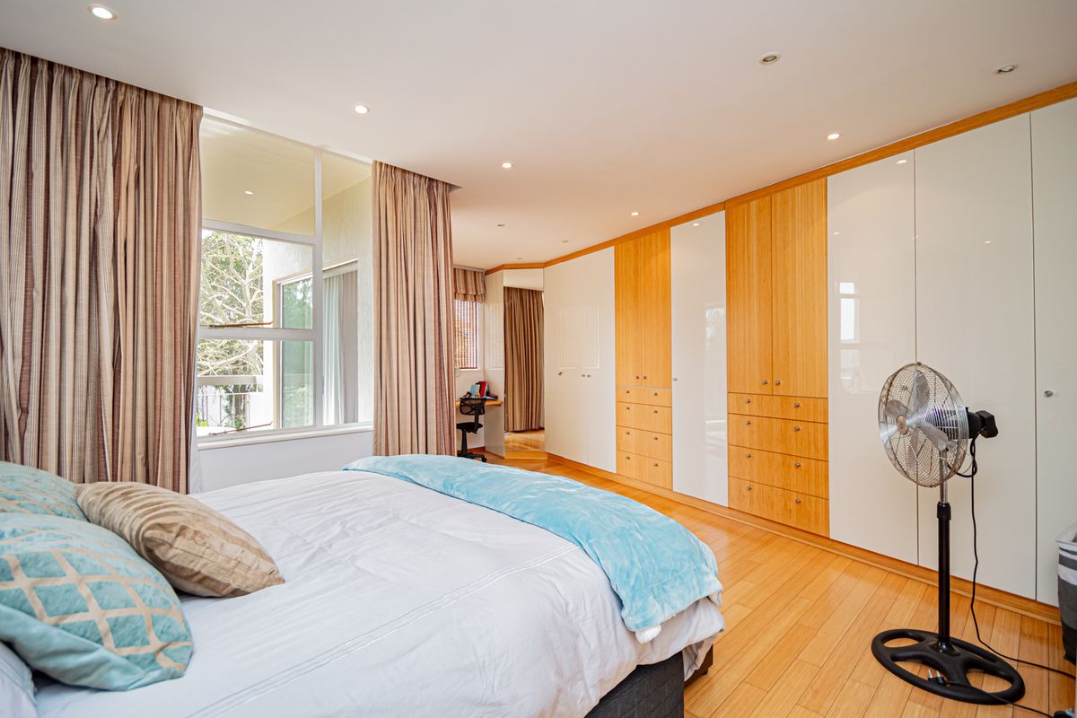 Spacious bedroom featuring extensive built-in cabinetry with a mix of wood and white finishes, hardwood flooring, and large windows providing natural light.