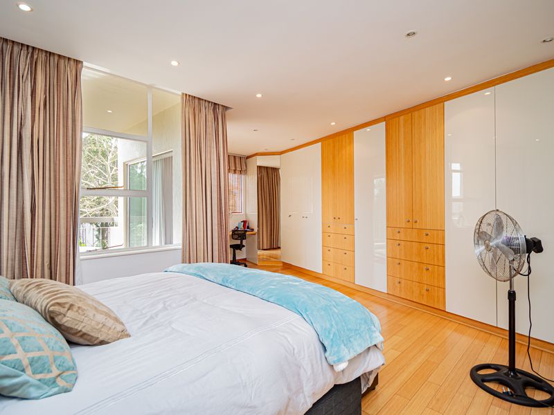 Spacious bedroom featuring extensive built-in cabinetry with a mix of wood and white finishes, hardwood flooring, and large windows providing natural light.