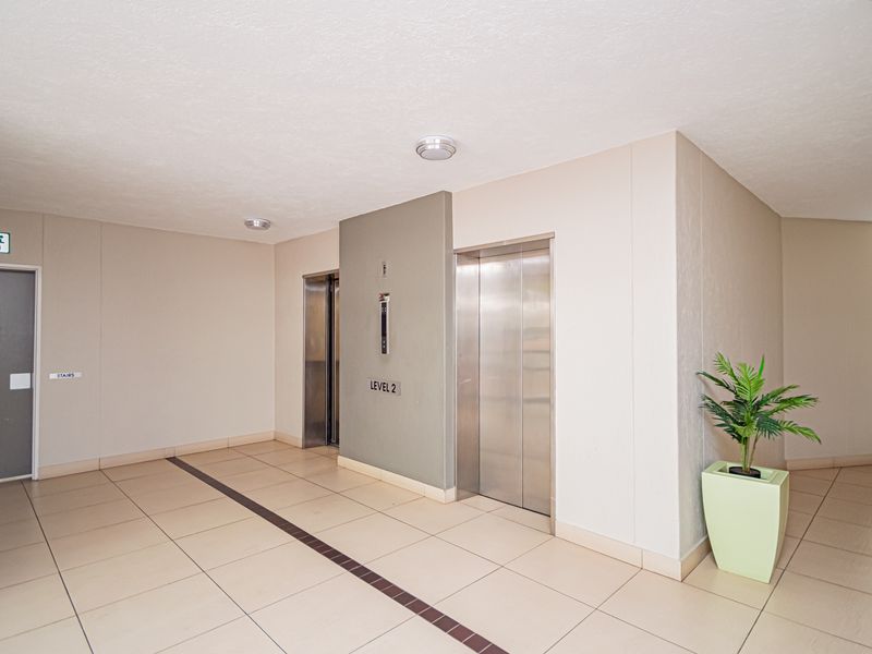 A clean and well-maintained apartment building hallway featuring tiled flooring, elevator access, and clear signage for fire exits.