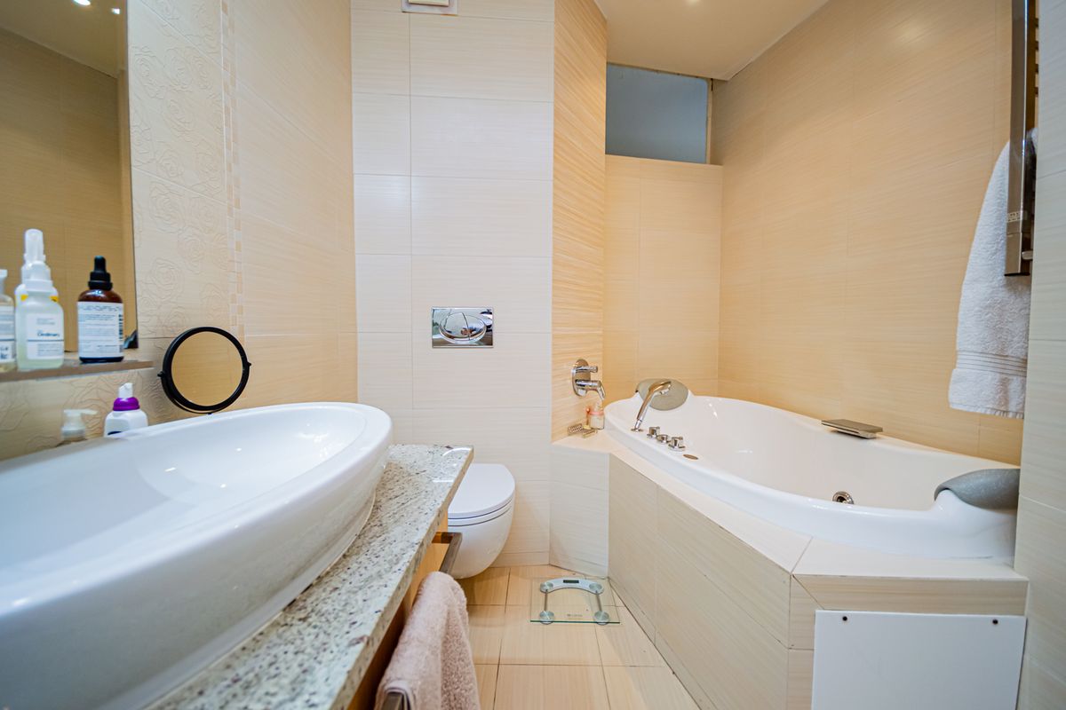A well-maintained bathroom featuring a built-in bathtub, wall-mounted toilet, and a vessel sink set on a granite vanity countertop with neutral wall tiling.