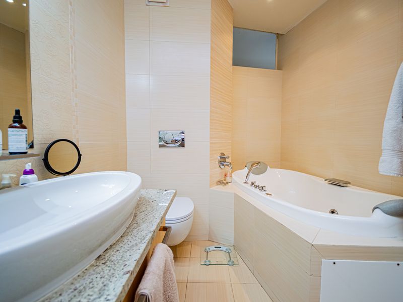 A well-maintained bathroom featuring a built-in bathtub, wall-mounted toilet, and a vessel sink set on a granite vanity countertop with neutral wall tiling.
