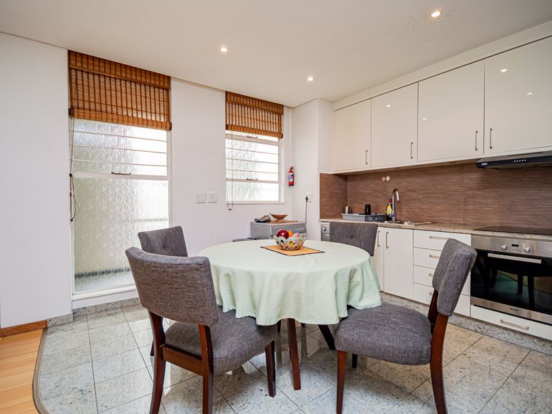Open-plan kitchen and dining area featuring modern white cabinetry, integrated appliances, tiled flooring, and natural light from large windows.