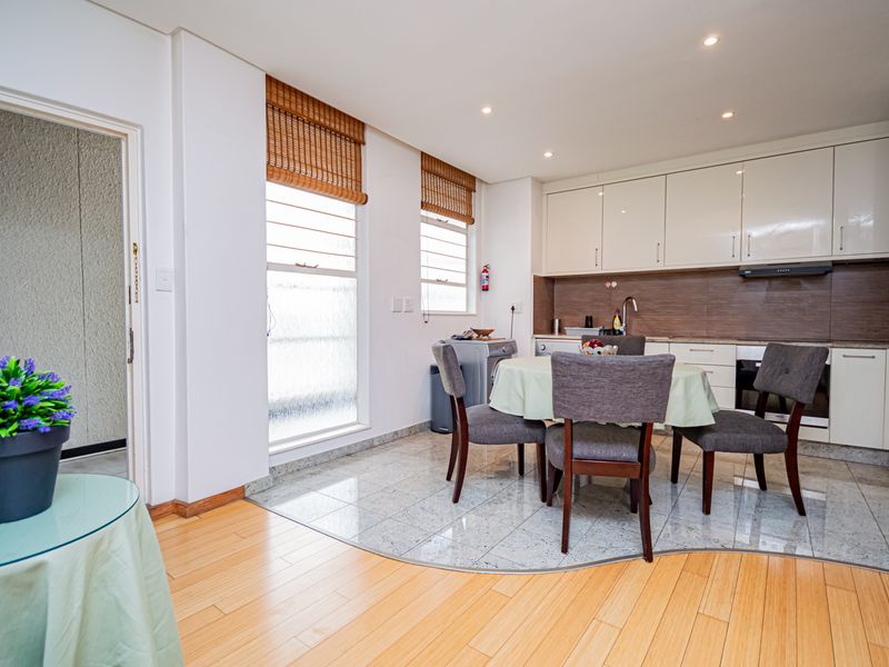 Open-plan kitchen and dining area featuring modern cabinetry, integrated appliances, tiled and laminate flooring, and natural light through large windows.