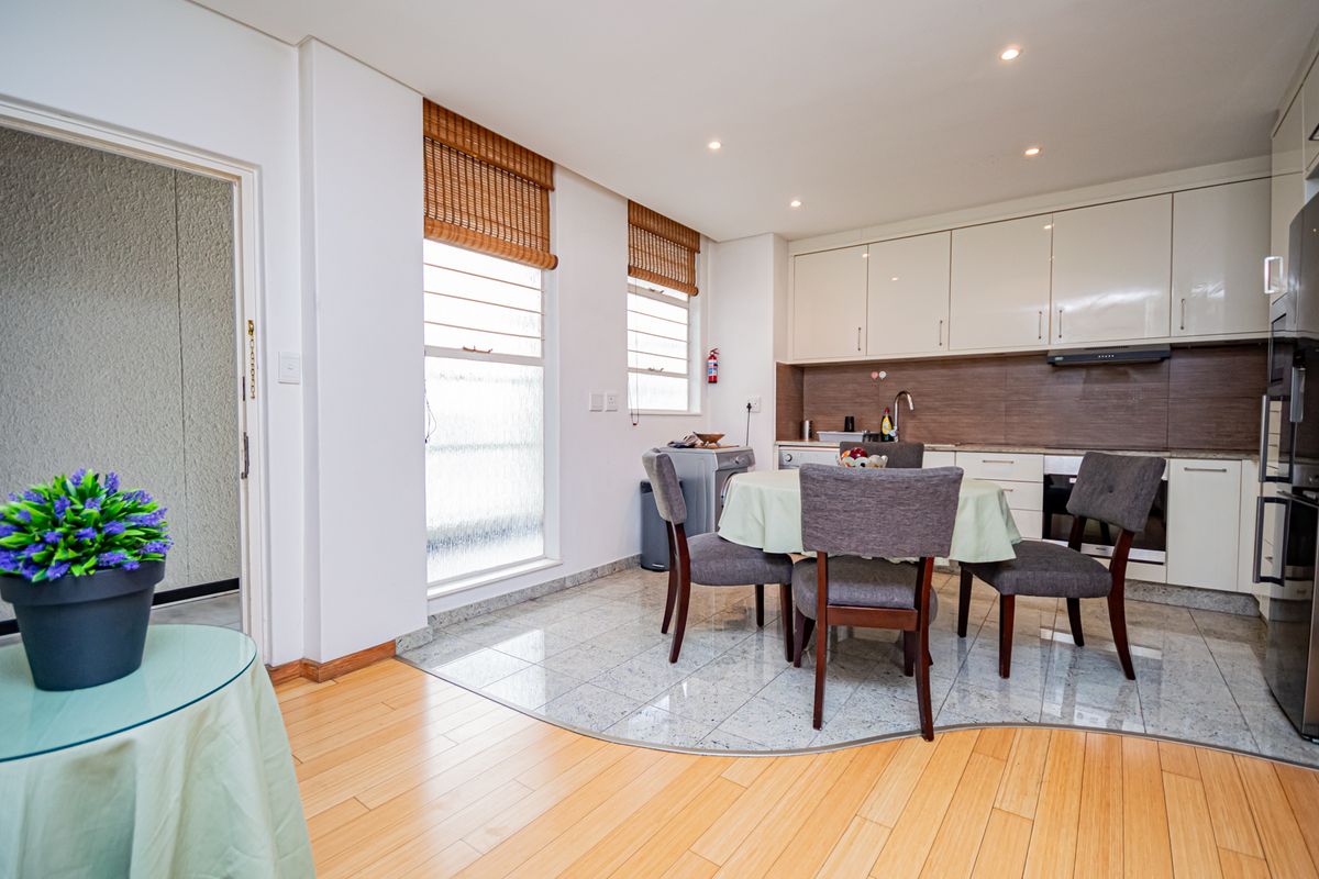 Open-plan kitchen and dining area featuring modern cabinetry, integrated appliances, tiled and laminate flooring, and natural light through large windows.