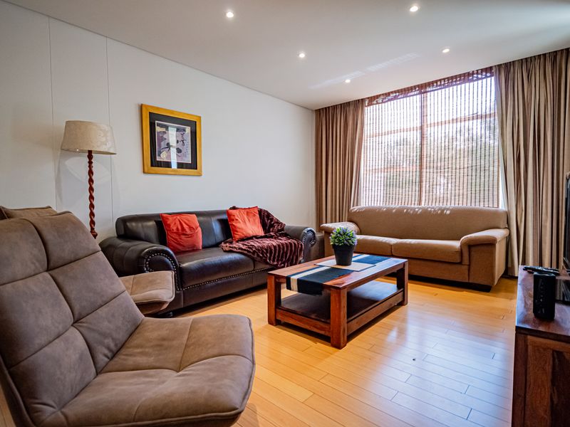 A well-maintained living room featuring hardwood flooring, recessed downlighting, and a large window with integrated curtain tracks.