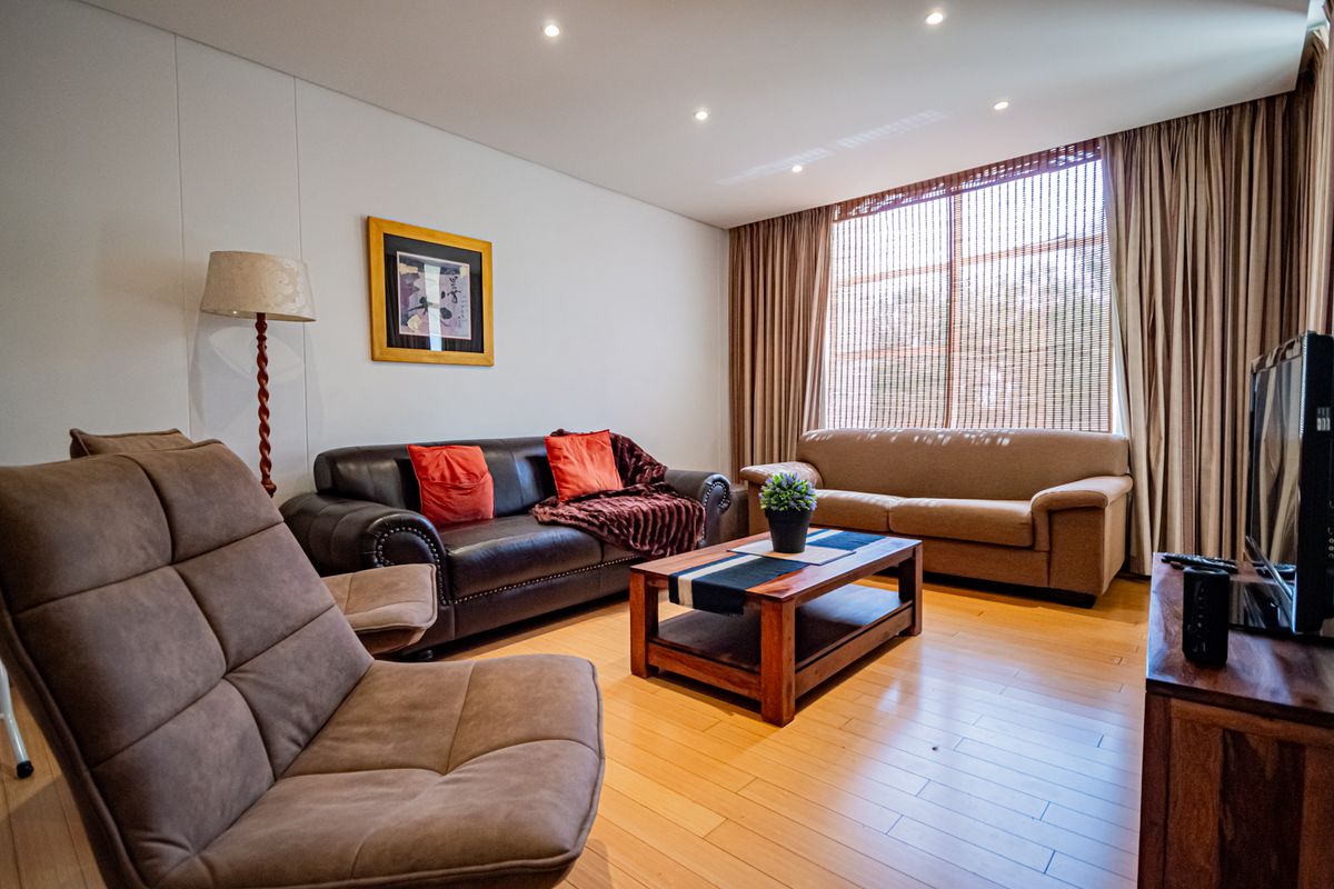 A well-maintained living room featuring hardwood flooring, recessed downlighting, and a large window with integrated curtain tracks.