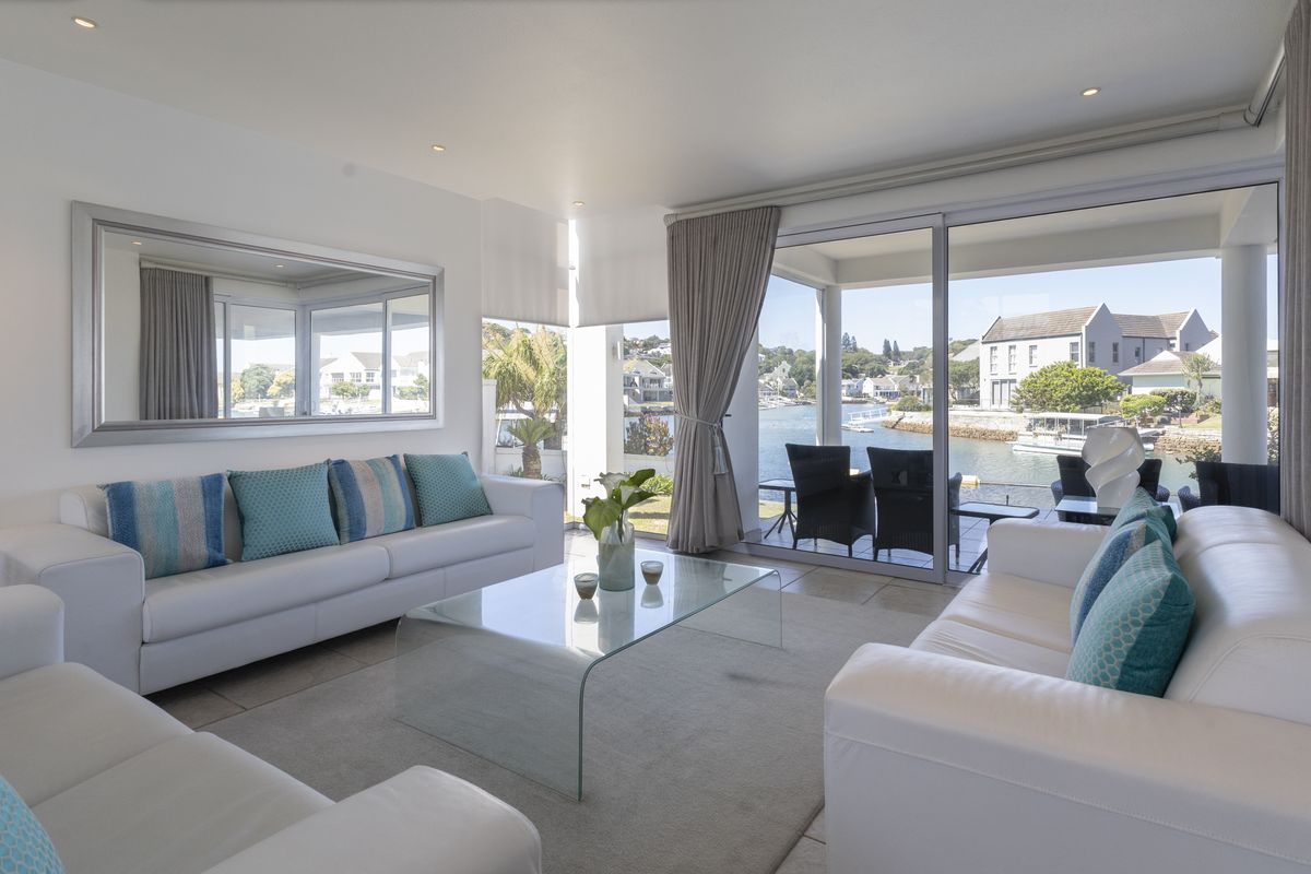 Bright and modern living room featuring large sliding glass doors that open to a scenic waterfront patio, offering excellent natural light and views.