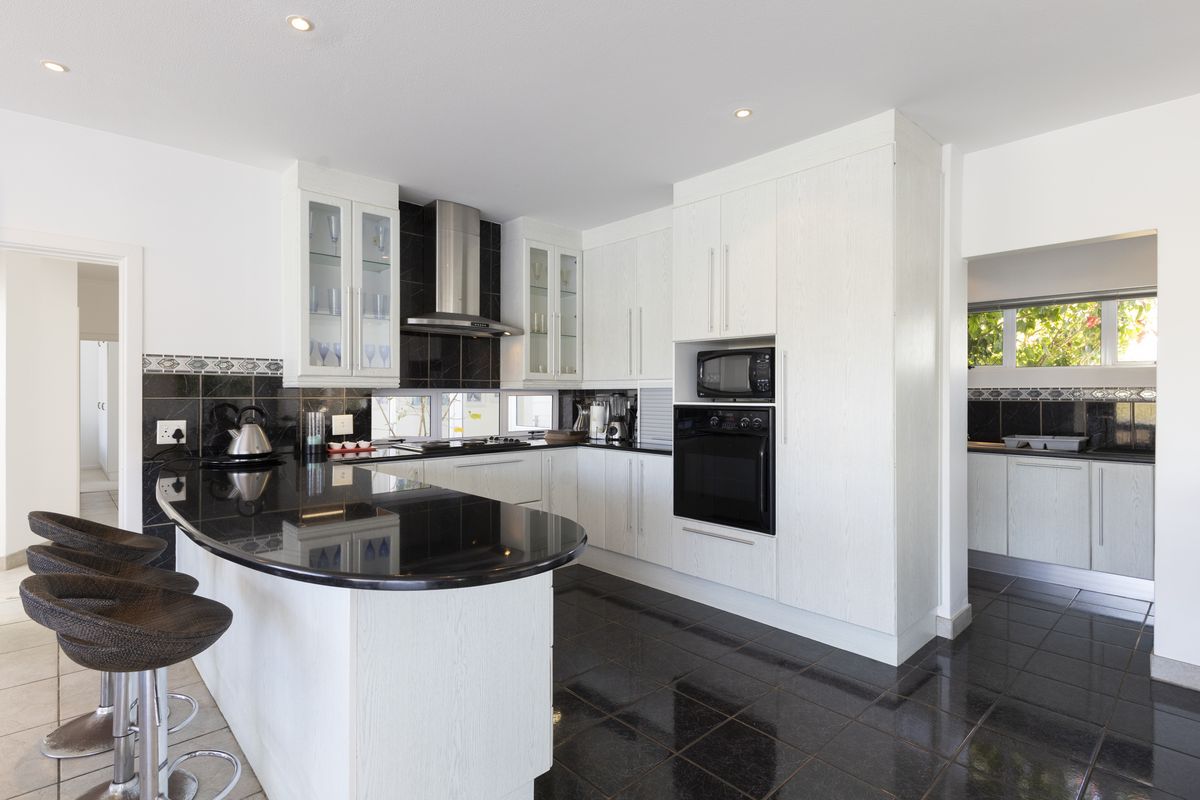 Modern kitchen featuring white cabinetry, black granite countertops, built-in appliances, and a breakfast bar, complemented by dark tiled flooring and a tiled backsplash.