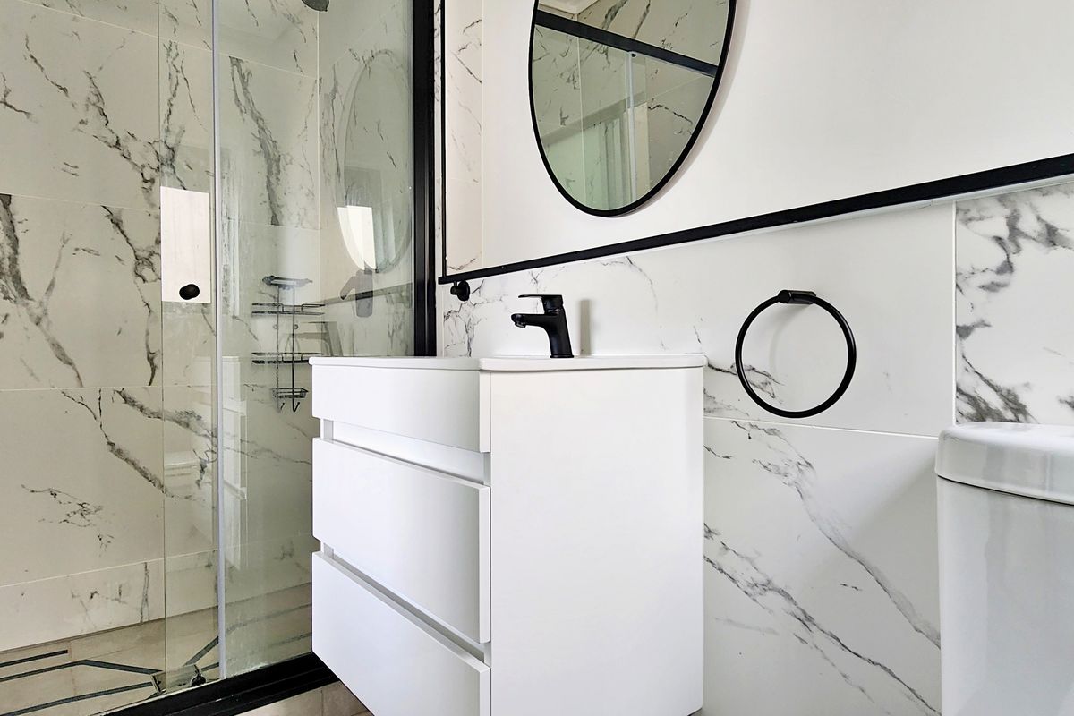 Modern bathroom featuring marble-look wall tiles, a sleek glass shower enclosure with black framing, a contemporary vanity, and stylish black fixtures.