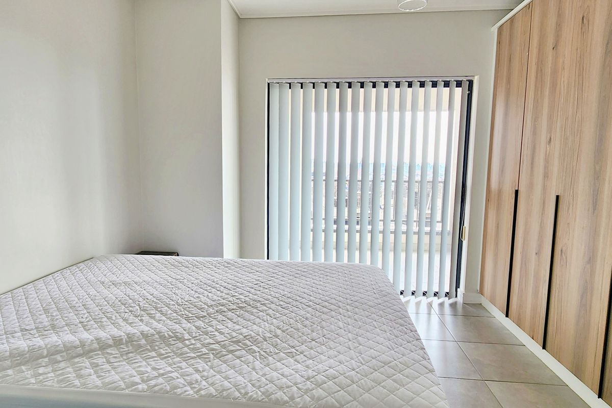 A bright bedroom featuring modern wood-finish built-in cupboards, tiled flooring, and vertical blinds leading to an outdoor area.
