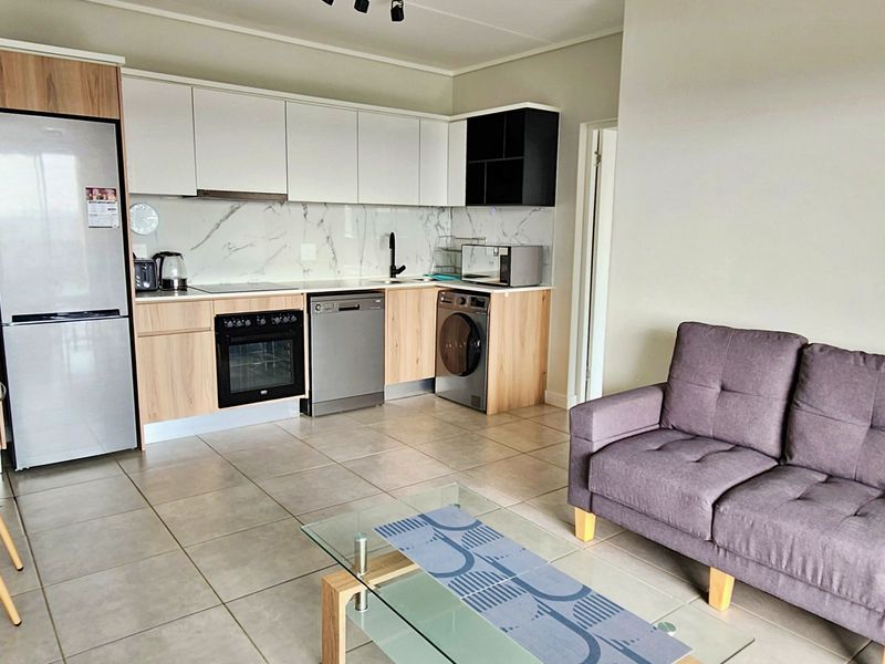 Modern open-plan living area featuring a contemporary kitchen with marble-look splashback, integrated appliances, and neutral tiled flooring throughout.