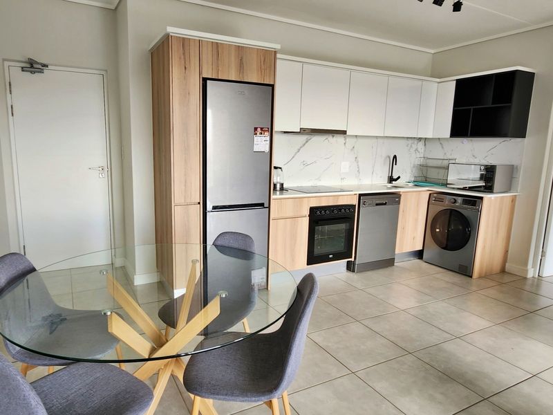 Modern open-plan kitchen featuring sleek two-tone cabinetry, stone-look backsplash, and integrated appliances, seamlessly flowing into the dining area with tiled flooring throughout.