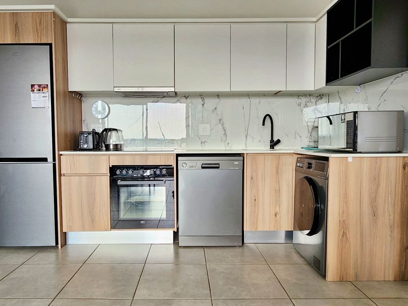 Modern kitchen featuring wood-grain and white cabinetry, marble-look splashback, integrated oven, and tiled flooring in a clean, contemporary apartment setting.