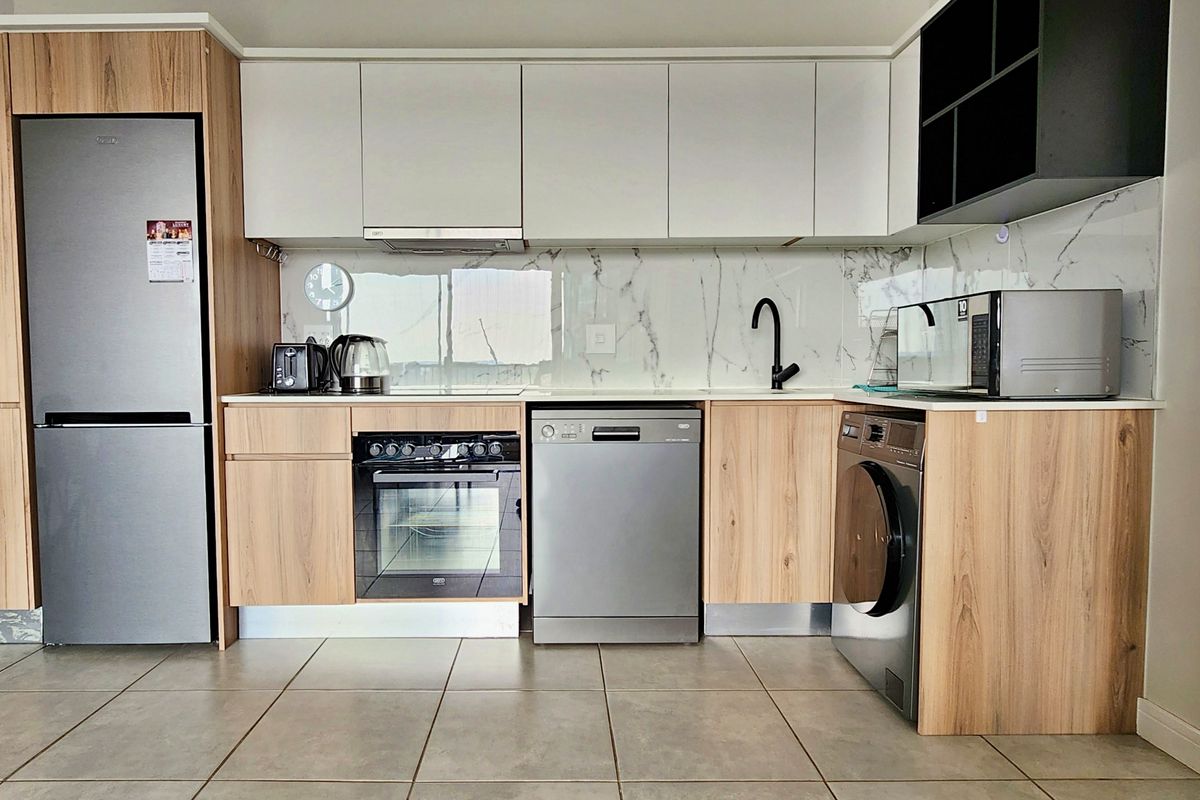 Modern kitchen featuring wood-grain and white cabinetry, marble-look splashback, integrated oven, and tiled flooring in a clean, contemporary apartment setting.