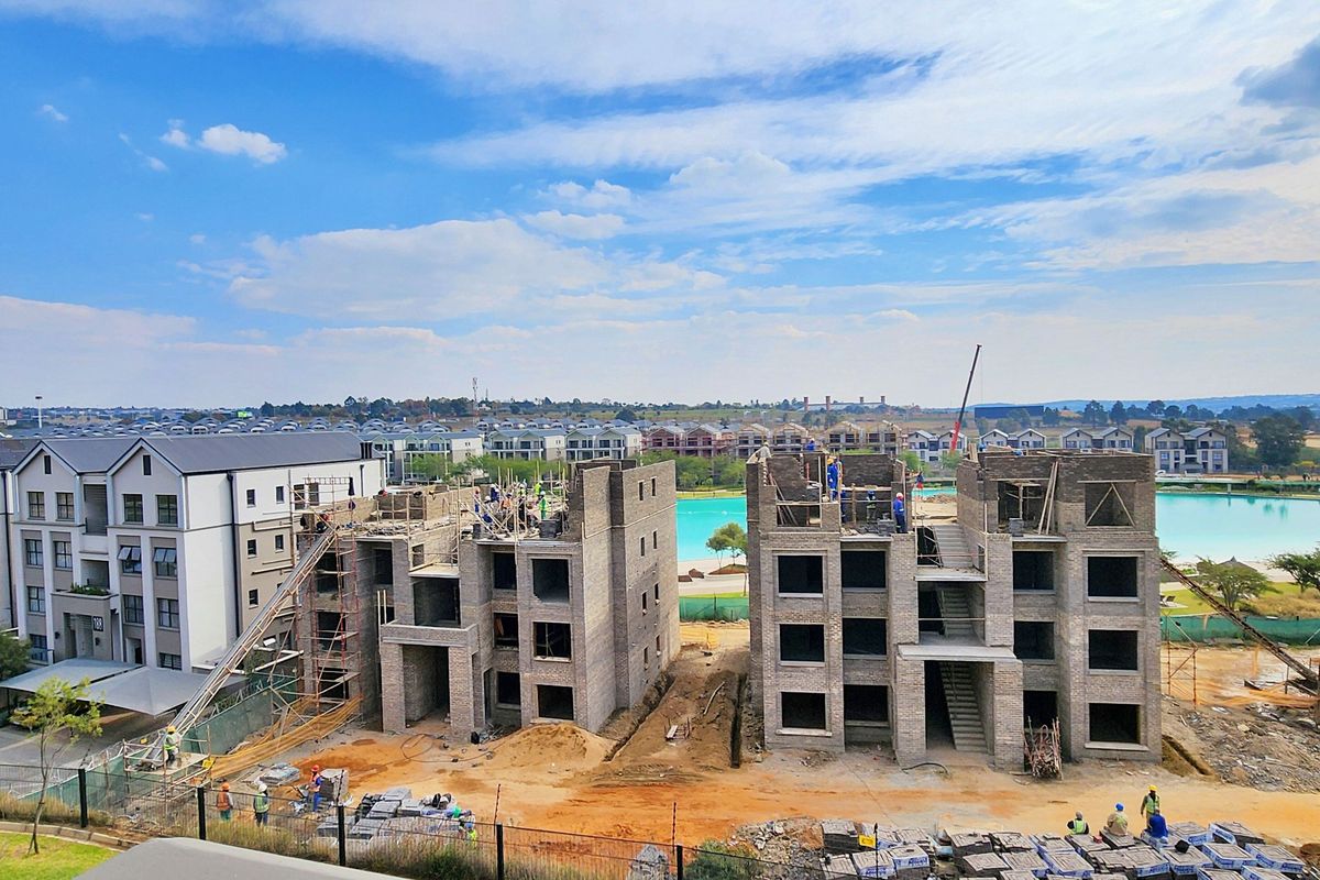 Aerial view of an apartment complex development site featuring multi-story buildings under construction and a large man-made lagoon in the background.
