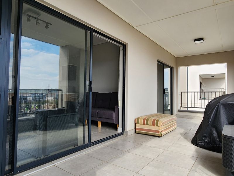A spacious covered balcony featuring tiled flooring, modern sliding glass doors, and a secure metal balustrade, offering a clean and functional outdoor living space.