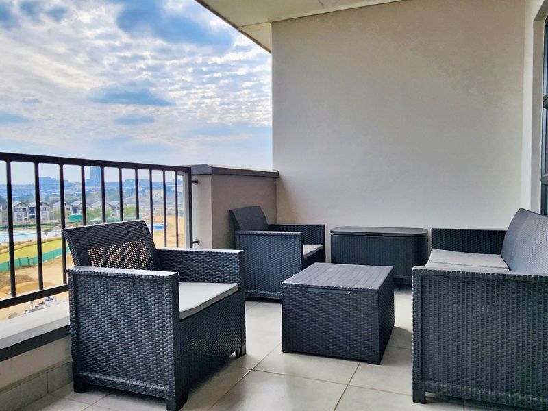 A covered balcony featuring tiled flooring, a metal balustrade, and a sliding glass door, offering an open view of the surrounding area.