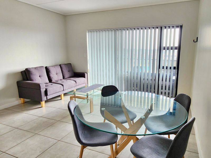 An open-plan living and dining area featuring neutral tiled flooring and large sliding glass doors with vertical blinds for natural light control.