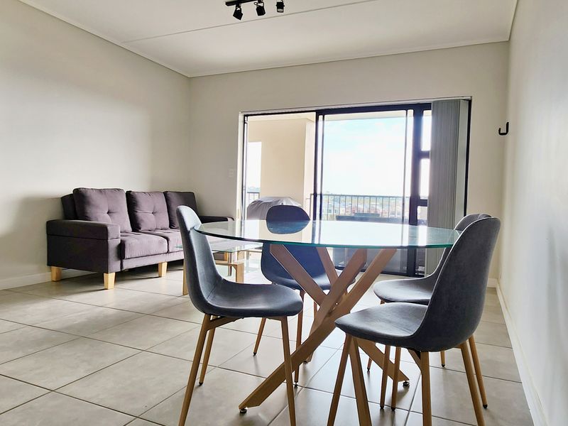 Open-plan living and dining area featuring neutral tiled flooring and large sliding glass doors leading to a balcony.