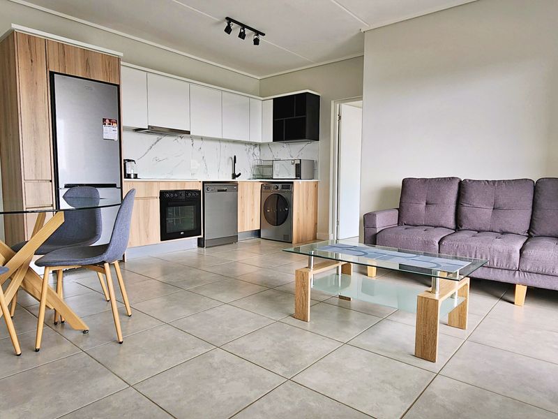 Modern open-plan living area featuring a contemporary kitchen with marble-look splashback, integrated appliances, and neutral ceramic floor tiles throughout.
