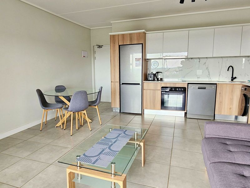 Modern open-plan living area featuring a contemporary kitchen with wood-tone and white cabinetry, marble-look splashback, and tiled flooring throughout.