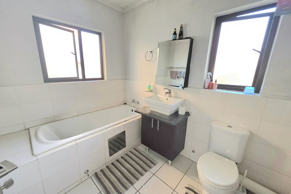 A functional bathroom featuring a built-in bathtub, a vanity cabinet with a vessel sink, and a standard toilet with tiled finishes throughout.