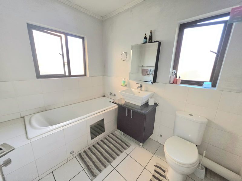 A functional bathroom featuring a built-in bathtub, a vanity cabinet with a vessel sink, and a standard toilet with tiled finishes throughout.