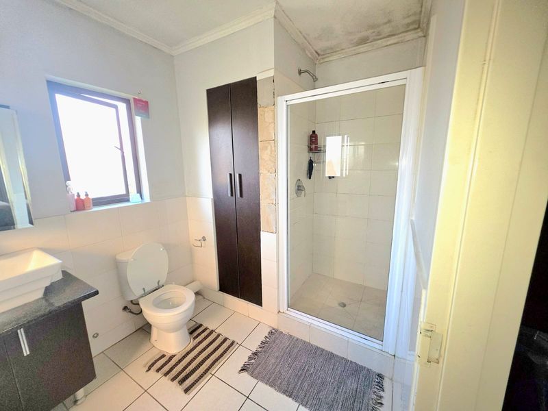 A functional bathroom featuring a shower enclosure, toilet, and vanity basin, requiring cosmetic attention to the ceiling and wall tiling.