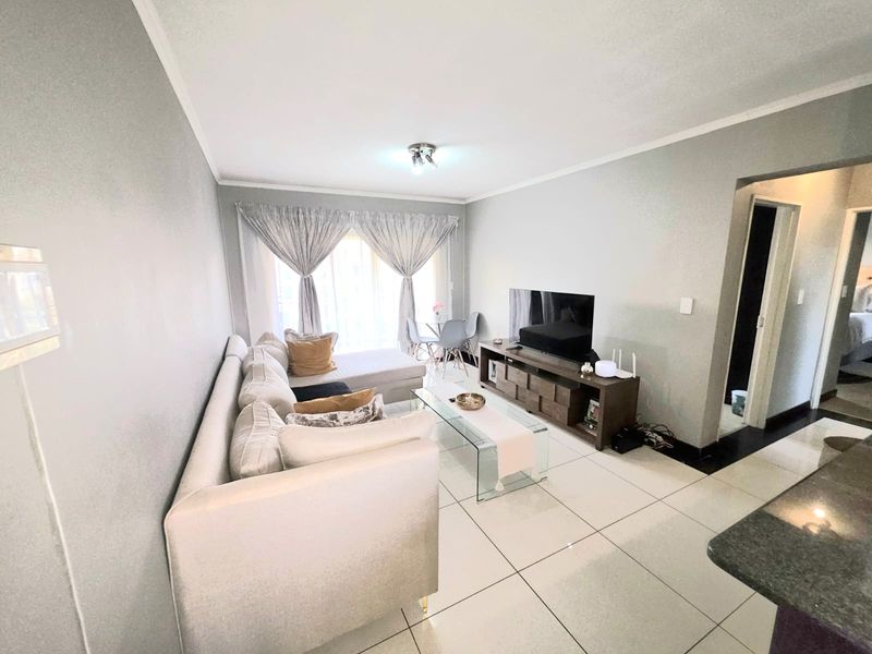 A bright and well-maintained living room featuring large format floor tiles and a sliding glass door providing access to the outdoor area.