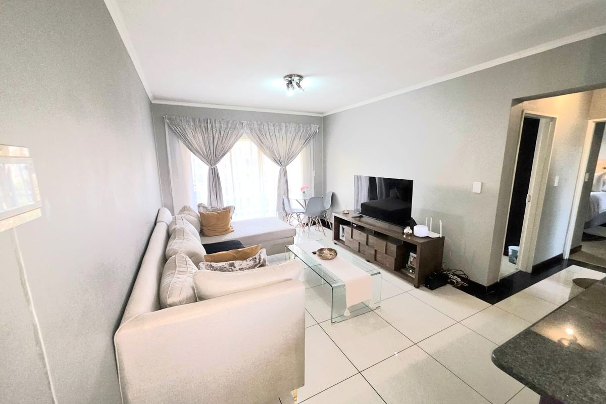 A bright and well-maintained living room featuring large format floor tiles and a sliding glass door providing access to the outdoor area.