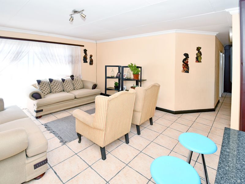 A spacious living room featuring neutral tiled flooring, coved ceilings, and track lighting, offering a comfortable and functional layout for relaxation.