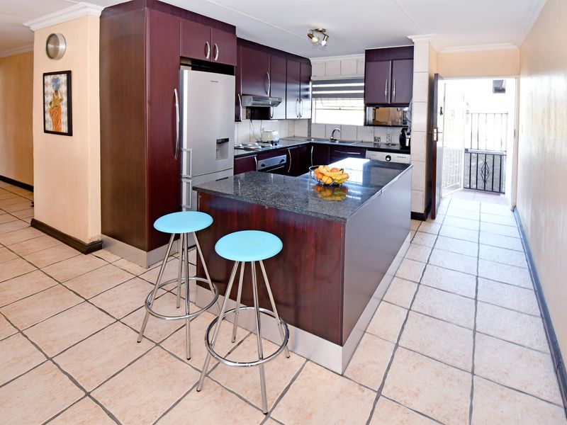 A functional kitchen featuring dark wood cabinetry, granite countertops, a central island, and tiled flooring, with direct access to an outdoor area.