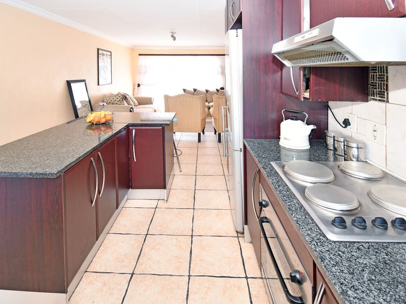 Open-plan kitchen and living area featuring dark wood cabinetry, granite countertops, built-in cooking appliances, and tiled flooring throughout.