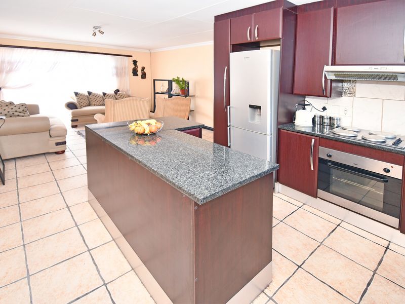 Open-plan living area featuring a kitchen with dark wood cabinetry, granite island, built-in oven, and hob, flowing into a tiled lounge space.