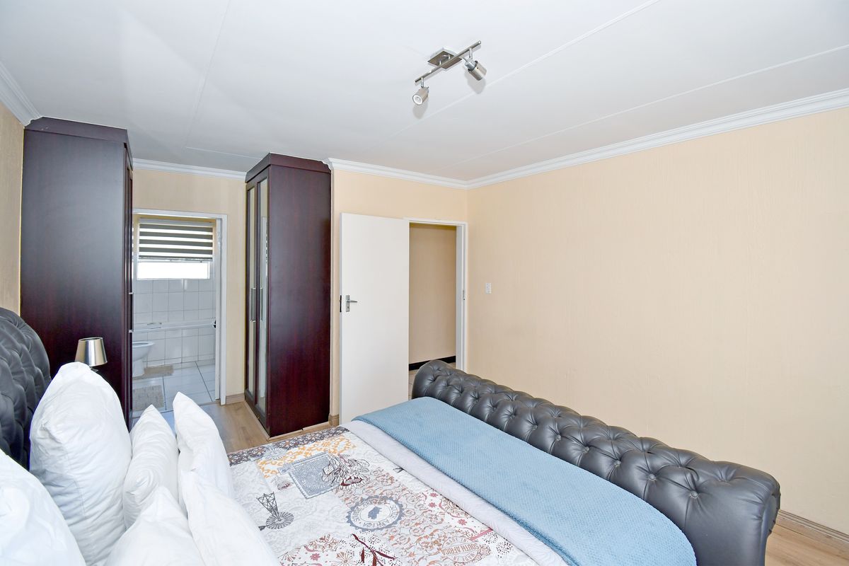 A bedroom featuring laminate flooring, coving, and a built-in wardrobe, with an adjoining bathroom visible through the doorway.